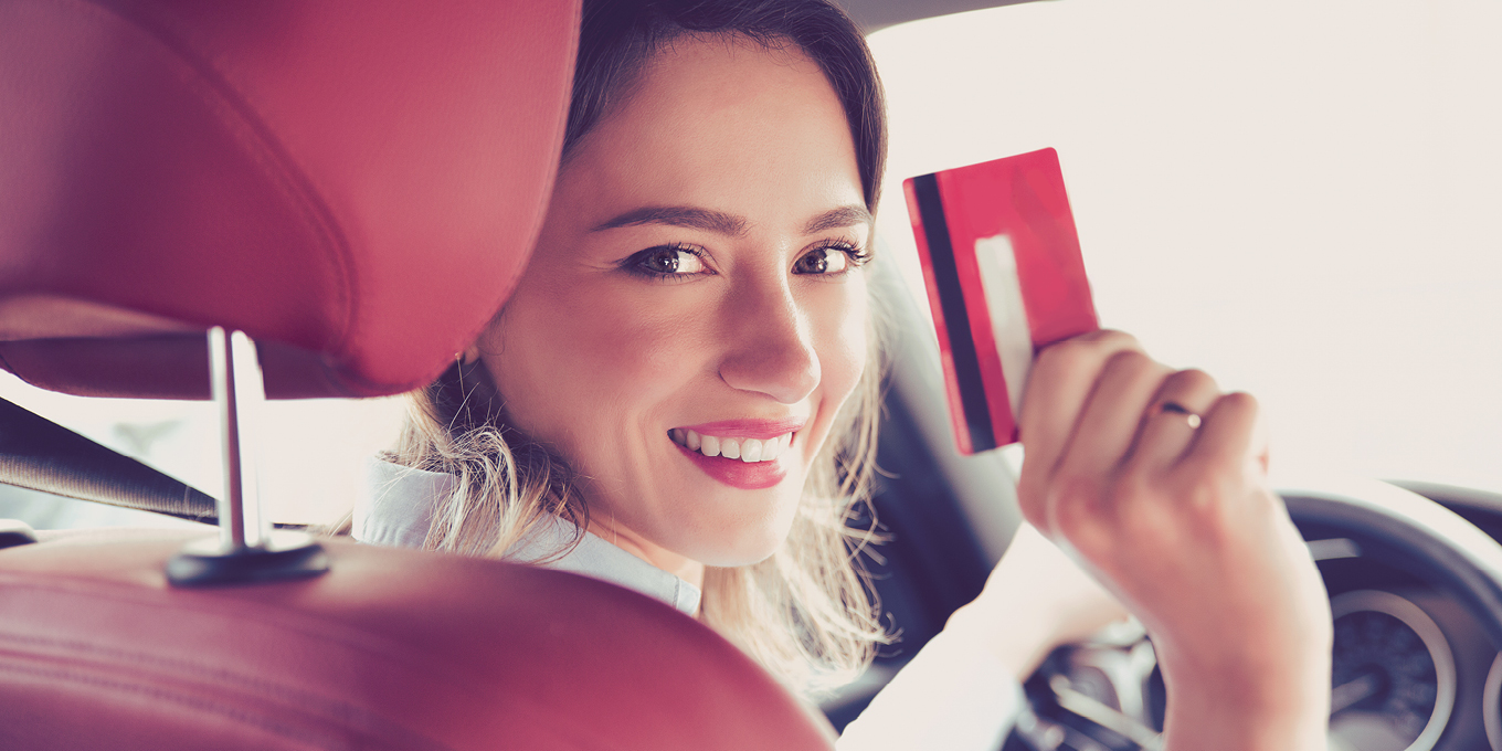 Smilende kvinne i bil som holder Circle K EXTRA Mastercard