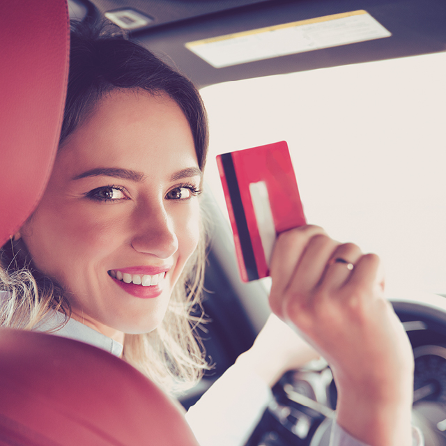 Smilende kvinne i bil som holder Circle K EXTRA Mastercard