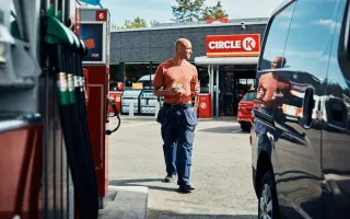 Man walking back to his vehicle at a Circle K station, with a sandwich and coffee in hand